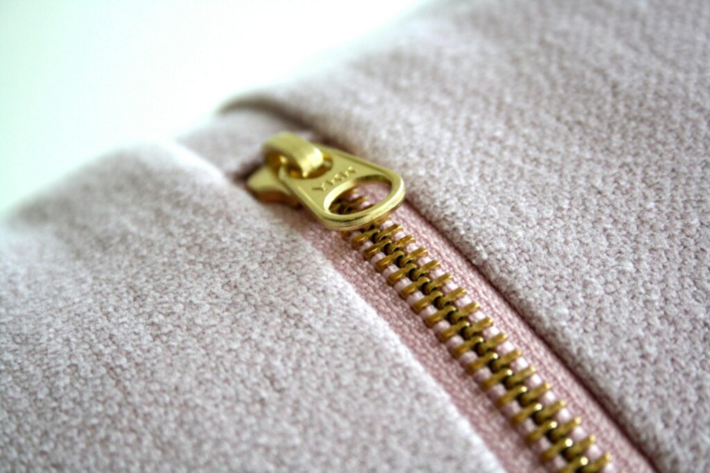 Detail of a gold zipper on a soft pink textile, highlighting fashion and design elements.